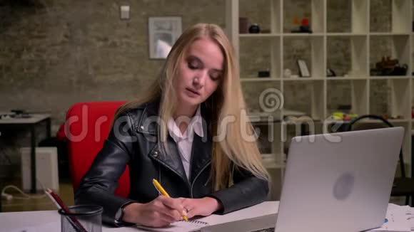 漂亮的白种人金发女人在工作场所坐直一边看电脑屏幕一边写下笔记视频的预览图