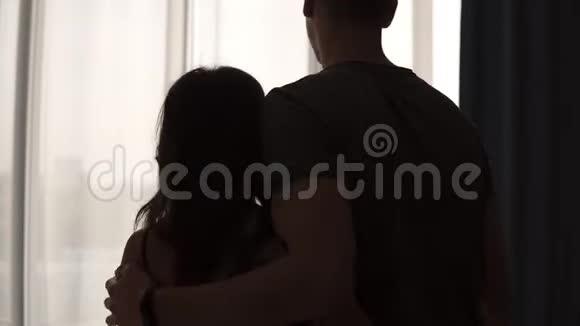 情侣们喜欢走到窗外拉开窗帘高加索男人和女人站在晨间卧室的后视镜视频的预览图