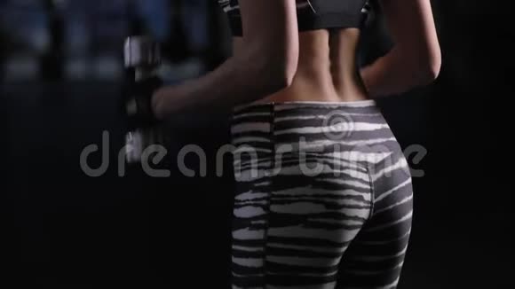 美丽的女人在健身房为二头肌举哑铃后视视频的预览图