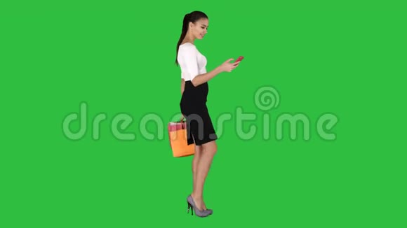 年轻女子带着购物袋在绿色屏幕上的手机上交谈Chroma键视频的预览图