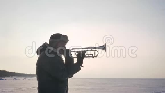 在冰冻的自然背景下独自一个高加索音乐家在阳光下吹喇叭的肖像视频的预览图