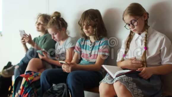 一个可爱的女学生正坐在同学旁边的长凳上看书其他孩子玩他们的视频的预览图