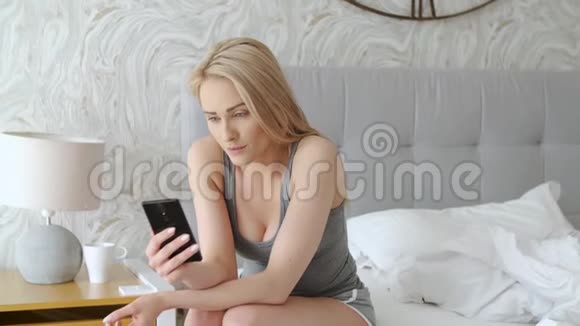 漂亮的中年女人早上坐在床上检查智能手机视频的预览图