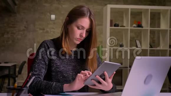 漂亮的白种人姜女在办公室背景下用平板电脑聊天微笑视频的预览图