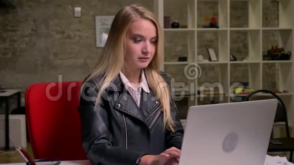 漂亮的金发白种人女孩坐在砖房里专心致志地看着电脑屏幕视频的预览图