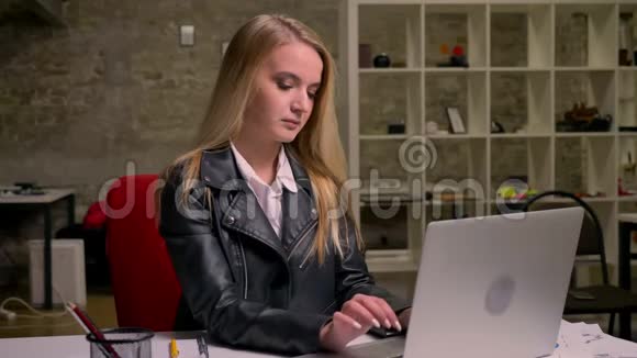 白种人金发认真工作的女孩坐在砖头办公室在桌面上使用她的电脑的录像视频的预览图