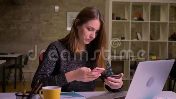 白人年轻女性使用智能手机和信用卡支付坐在办公室的笔记本电脑前视频的预览图