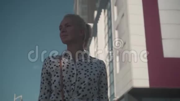 穿着白色衬衫的白人年轻商务女性站在现代办公楼附近的街道上穿着黑豌豆视频的预览图