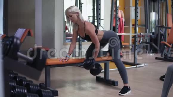 金发女人在一个现代健身房锻炼时她的哑铃重量很大各种设备都靠在长凳上视频的预览图