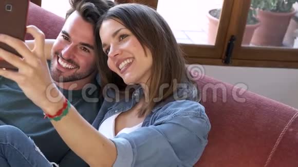 幸福的年轻夫妇在家坐在沙发上用智能手机自拍视频的预览图