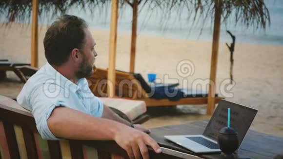 中镜头成功内容商人坐在异国情调海滩躺椅与笔记本电脑放松在海洋度假村视频的预览图