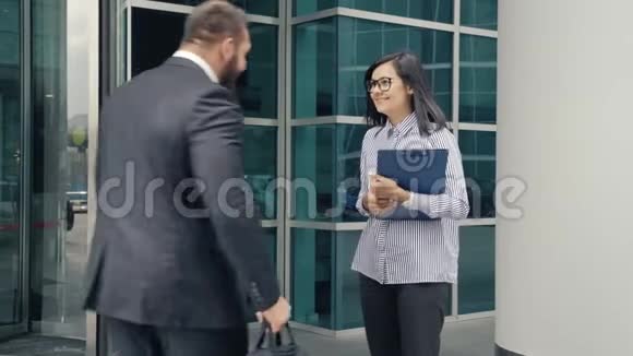 商务男士在办公楼入口处迎接一位年轻女士视频的预览图