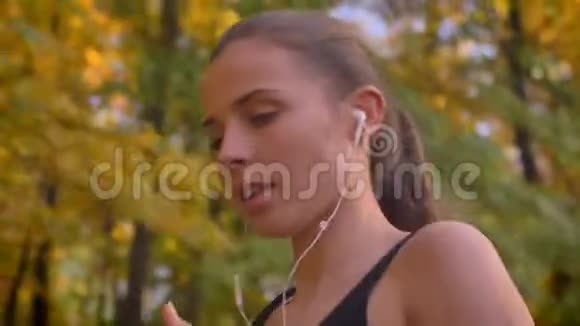 多莉从脸到胸特写照片的年轻白种人苗条女孩跑在秋季公园带耳机视频的预览图