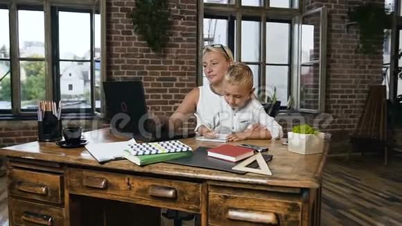 漂亮的中年女商人在笔记本电脑上工作当她可爱的小孙子在笔记本上写东西的时候视频的预览图