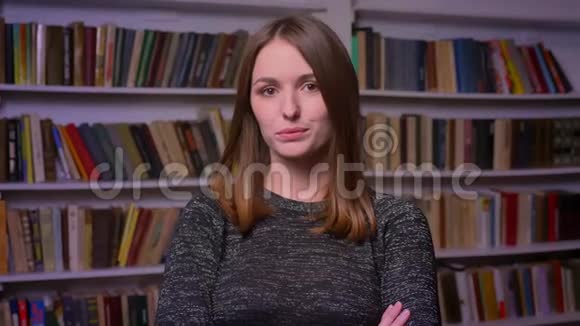 白人红头发的女学生严肃地看着镜头在书架背景上调情视频的预览图