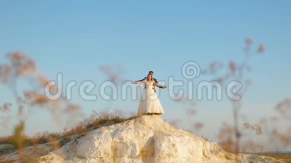 美丽的新娘和新郎站在山上在蓝天下翱翔微笑着情侣婚礼之旅视频的预览图