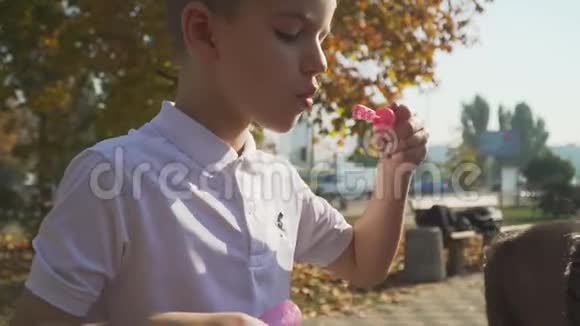 快乐的孩子在秋天公园吹肥皂泡男孩在户外和朋友玩慢动作视频的预览图