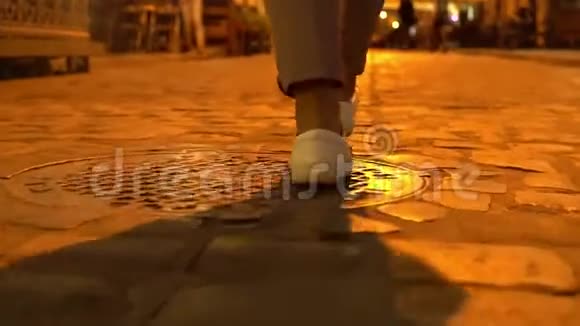 年轻女孩晚上穿着白色运动鞋穿过老城区视频的预览图