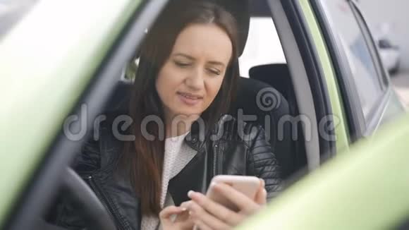 一个女人用智能手机站在停车场的车里视频的预览图