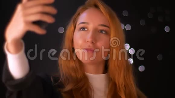 可爱的红发白种人女人手里拿着她的手机打着视频电话站在室内说话放松下来视频的预览图