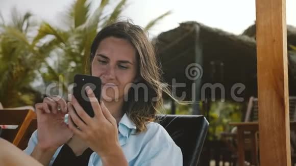 在异国度假胜地使用智能手机娱乐应用程序在海滩躺椅上休息的快乐轻松的旅游妇女视频的预览图