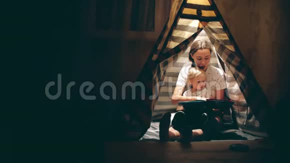 妈妈和她的小女儿晚上在一个小帐篷里一起读一本书视频的预览图