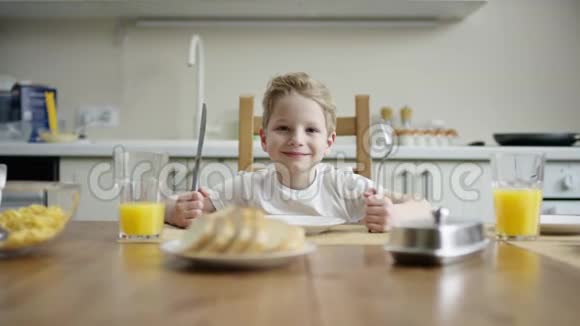 高兴的男孩坐着刀叉在午餐与一碗玉米片和等待款待视频的预览图