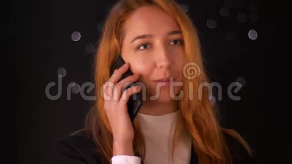 令人惊叹的白种人红头发的女人站在黑色背景下通过电话交谈积极地看着一边视频的预览图