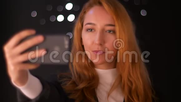 美丽的白种人女性正在手机上自拍同时站在黑暗的背景上与白色的埃斯庞特隔绝视频的预览图