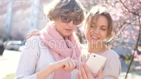 一个成年的女儿和她成熟的母亲站在街中央手里拿着一部智能手机视频的预览图