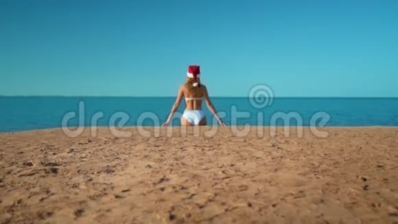 那个穿着白色泳衣戴着圣诞老人帽子的漂亮女孩坐在大海的背景上视频的预览图
