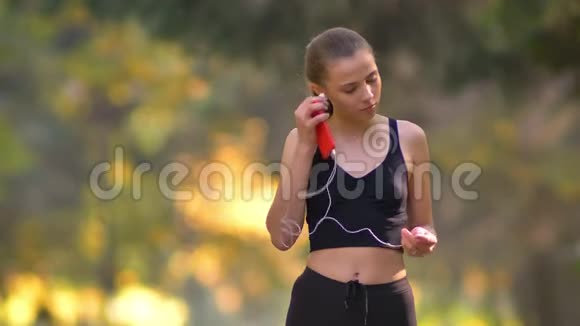 穿着连衣裙戴上耳机开始在秋季公园跑步的年轻女孩的特写照片视频的预览图