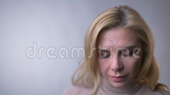 一位中年金发女士的特写肖像抬起眼睛在灰色背景上微笑成相机视频的预览图