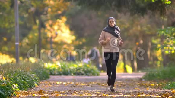 戴头巾的穆斯林妇女在秋日公园慢跑停下来检查手表继续跑步视频的预览图