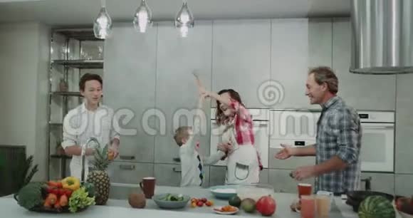 母亲和他9岁的儿子在现代化的厨房里跳舞父亲和16岁的男孩高兴地站在旁边视频的预览图