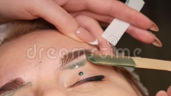 眉毛形状的蜡校正美容师在眉毛上涂上温暖的绿色蜡去除多余的头发视频的预览图