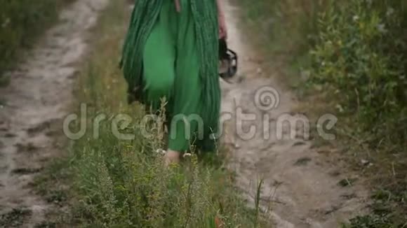 一个女人晚上赤脚走在绿草上一个年轻的女人正在散步慢动作视频的预览图