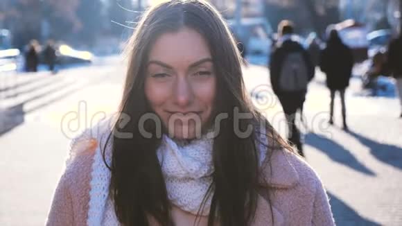 城市街道上身着时髦外套和围巾的满意黑发女人的肖像慢镜头微笑视频的预览图