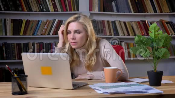 金发中年白种人妇女在办公室工作手提电脑和思考书架背景的肖像视频的预览图