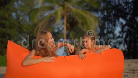 一个年轻女子和她的小儿子在沙滩上的充气沙发上玩耍的慢镜头视频的预览图