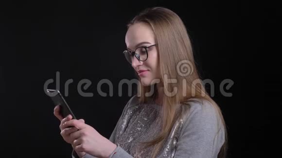 年轻迷人的时髦女性戴眼镜的特写镜头在手机上发短信背景与黑色隔离视频的预览图