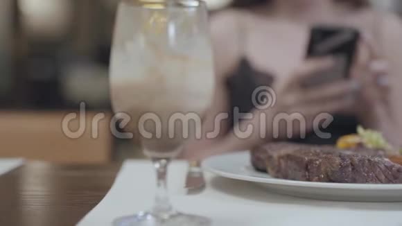 美味的牛排蔬菜和叶子躺在盘子里在餐厅的女人面前女士的手在发短信视频的预览图
