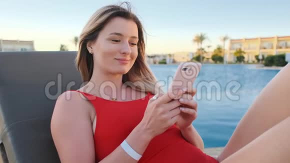 女人在海滩的躺椅上用手机穿着红色比基尼的夏天女孩上网发短信和滚动视频的预览图
