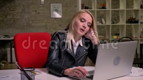 漂亮的白种人金发女性坐在桌面上放松在笔记本电脑和文件附近休息光线充足视频的预览图