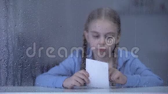 小女孩看着雨窗后的照片孤儿失踪的父母视频的预览图