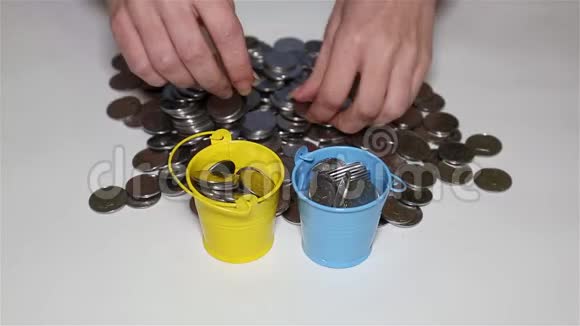 女孩的手把硬币放进五颜六色的小桶里视频的预览图