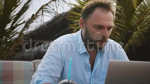 快乐的中年创意自由职业者男子用笔记本电脑在棕榈树下在线工作的特写镜头视频的预览图