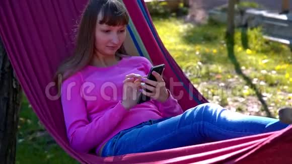 女孩在吊床上用手机发短信视频的预览图