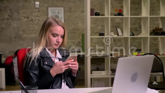 可爱的金发白种人女商人在工作场所的红椅上轻松地转动手机视频的预览图