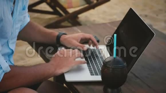 特写镜头的男性商人手使用笔记本电脑与花式饮料在异国情调的夏季海洋度假海滩工作视频的预览图